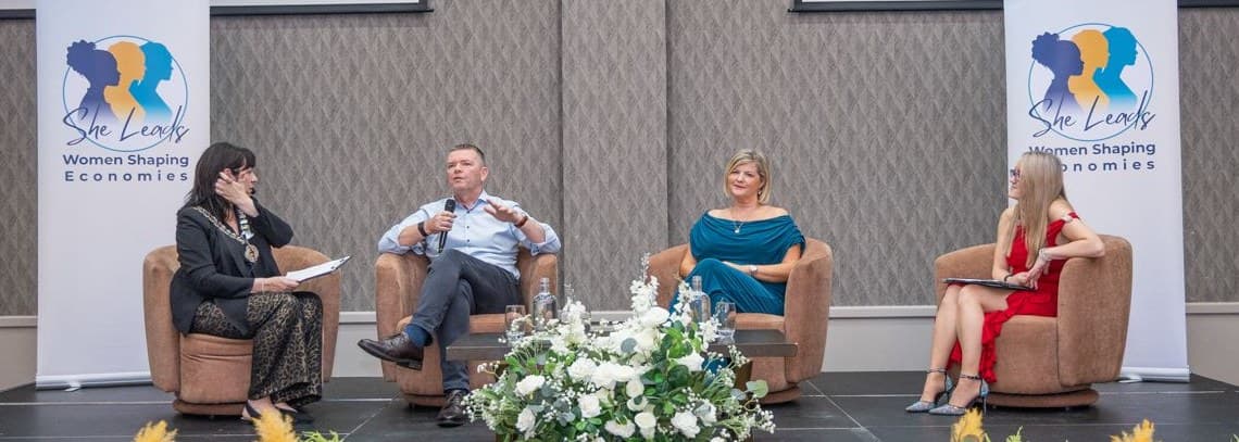 Barry James speaking on a panel at the She Leads event, with three other panellists.